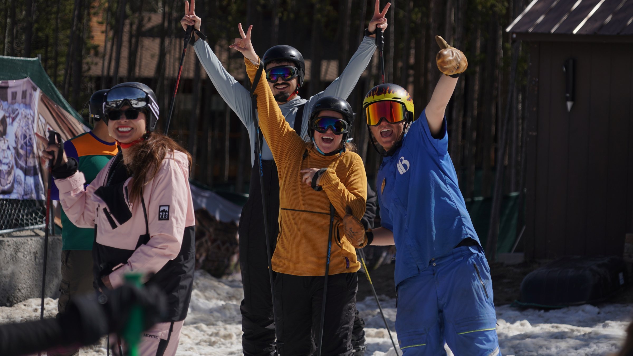 Friends in ski gear raising their arms on the snow